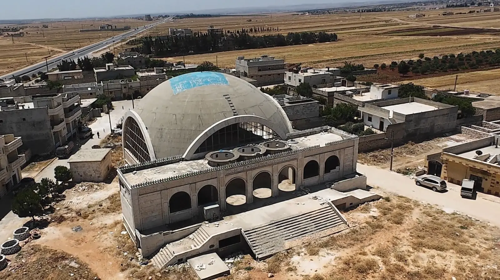 Aerial view of the domed Ibadur Rahman Masjid in Dayr Jamal, with the international highway running past the town