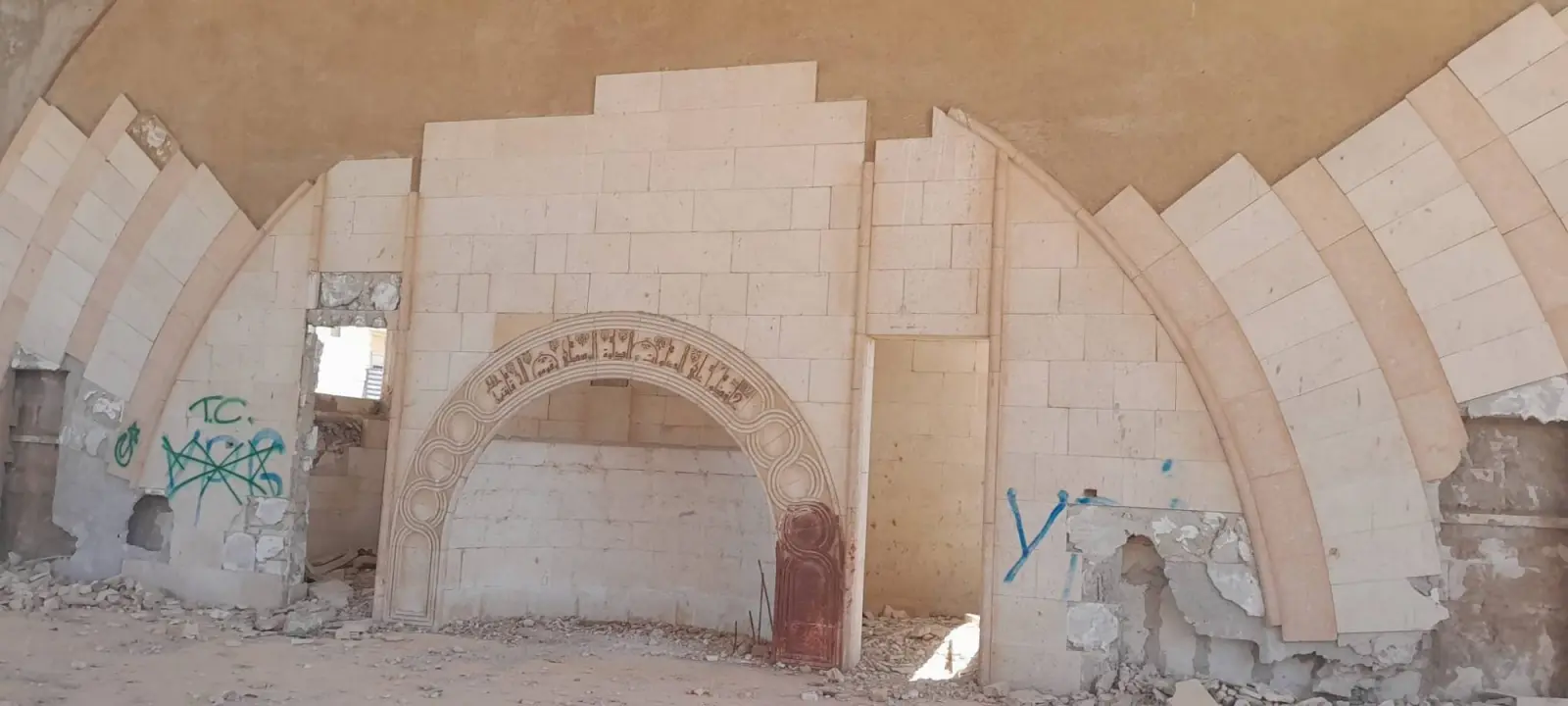 The mihrab wall inside the destroyed Ibadur Rahman Masjid, marked with graffiti and broken stone